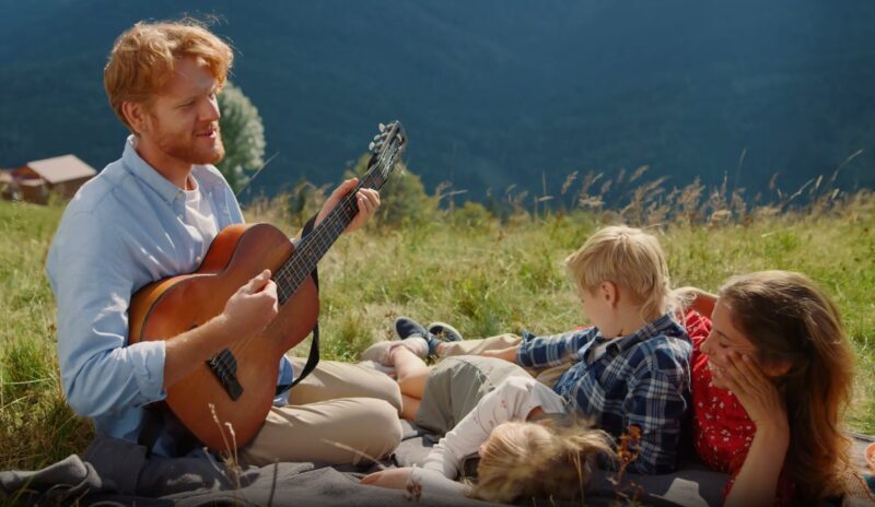 Family enjoying a vacation , they are on the grass while dad plays the guitar