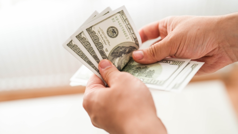 A person counts a stack of U.S. dollar bills by hand to keep track of personal finances