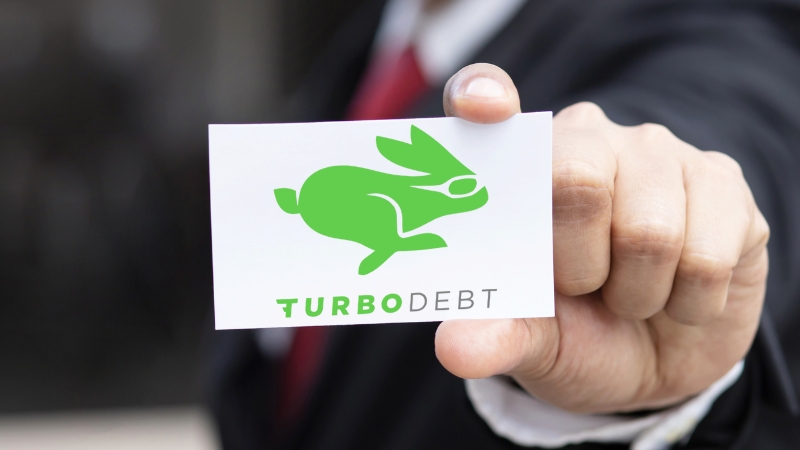 A person in a suit holds a business card with a green rabbit logo and the words Turbo Debt clearly printed on it