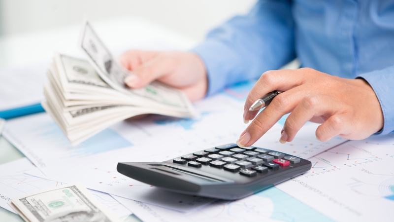 A person uses a calculator and counts money by hand at a desk with financial documents