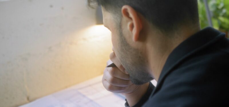 A man sitting at a desk, deeply focused on reading and analyzing a document while holding a pen