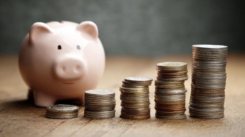 Piggy bank next to stacked coins arranged in ascending height, symbolizing growing savings