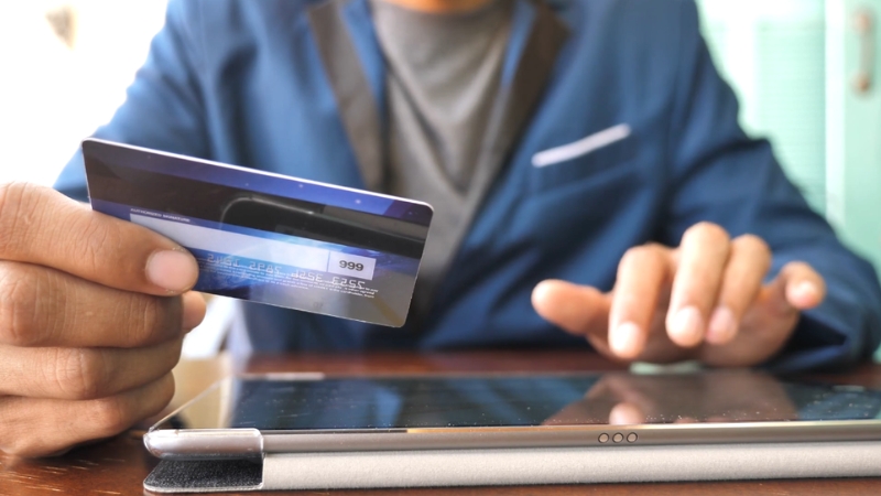 A person uses a credit card and tablet, showing concerns about how much debt settlement can drop a credit score