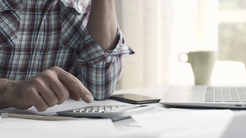A man calculates bills and expenses at a desk while managing payday loan debt paperwork