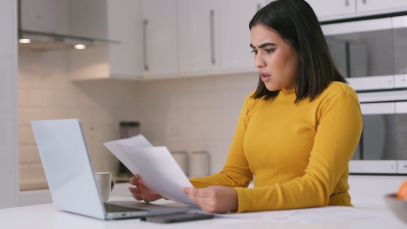 A concerned woman reviews bills and records loan details at her kitchen table