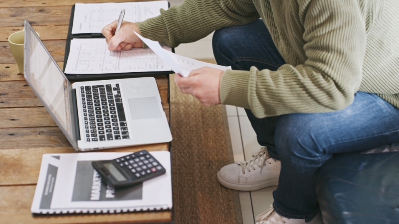 Person sitting at a table with a laptop, calculator, and papers, reviewing financial documents for debt consolidation planning