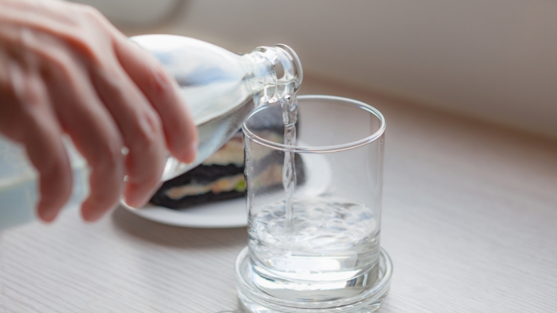 A hand pours fresh water into a clear glass on a table to support hydration and reduce anxiety