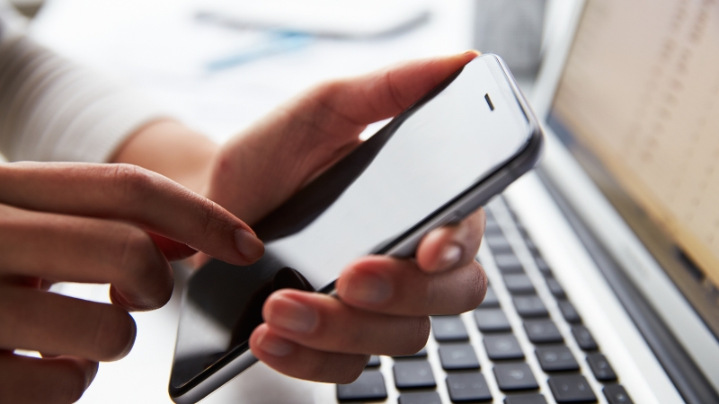A person holds a smartphone near a laptop, preparing to set it aside for a five-minute walk without distractions