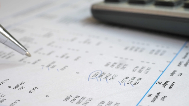 A pen points at figures on a credit report next to a calculator on a desk