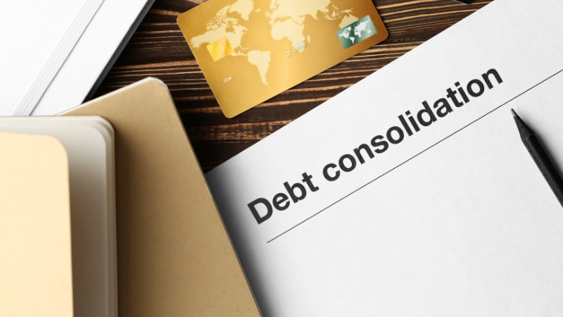 Paper labeled “Debt consolidation” on a desk with a credit card, folders, and a pen