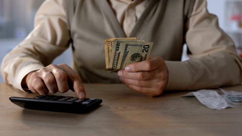 A person counts cash and uses a calculator at a table with receipts nearby