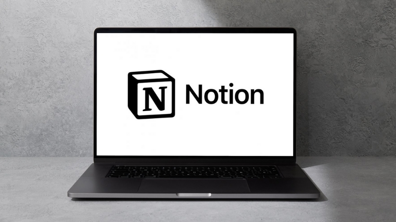 A laptop displays the Notion logo on a white screen against a gray wall background