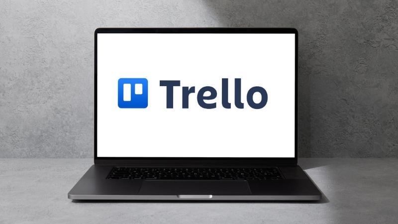 A laptop shows the Trello logo on the screen against a plain gray background