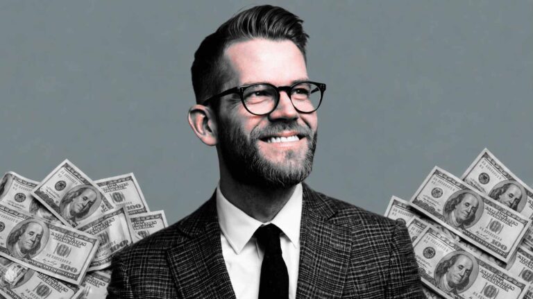 Smiling businessman in glasses with stacks of dollar bills in the background.